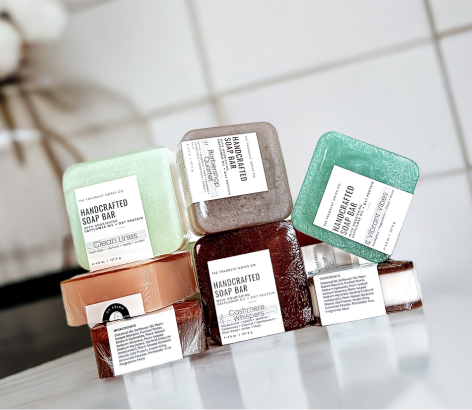 The Fragrant Notes Co. natural soap bars displayed on a white bathroom counter with plant in the background.