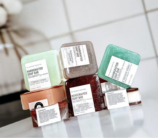 The Fragrant Notes Co. natural soap bars displayed on a white bathroom counter with plant in the background.