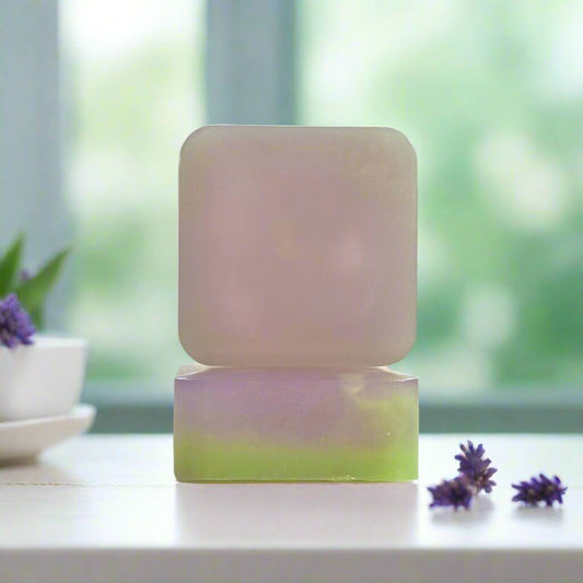 Purple Lavender Tea Time soap sitting in front of a bright window, surrounded by pieces of lavender.