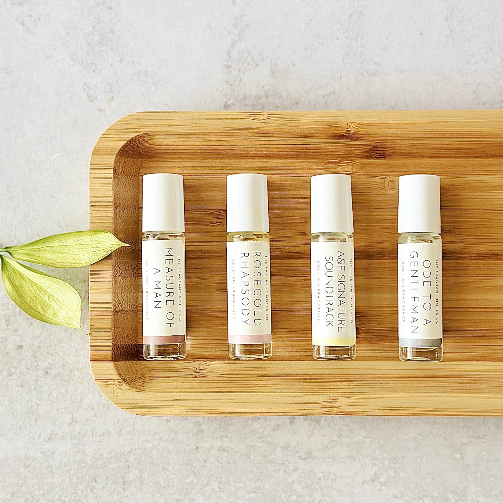 Signature scent roll-on perfume oils laying flat in a row on a wooden dish.